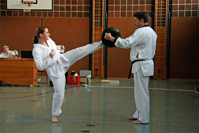 Fusstritt einer jungen Frau im Taekwondo-Anzug gegen eine
          Trainings-Bratze, die ein junger Mann im Trainingsanzug ihr
          hinhält, bei einem Kurs für Selbstverteidigung in Bad Tölz